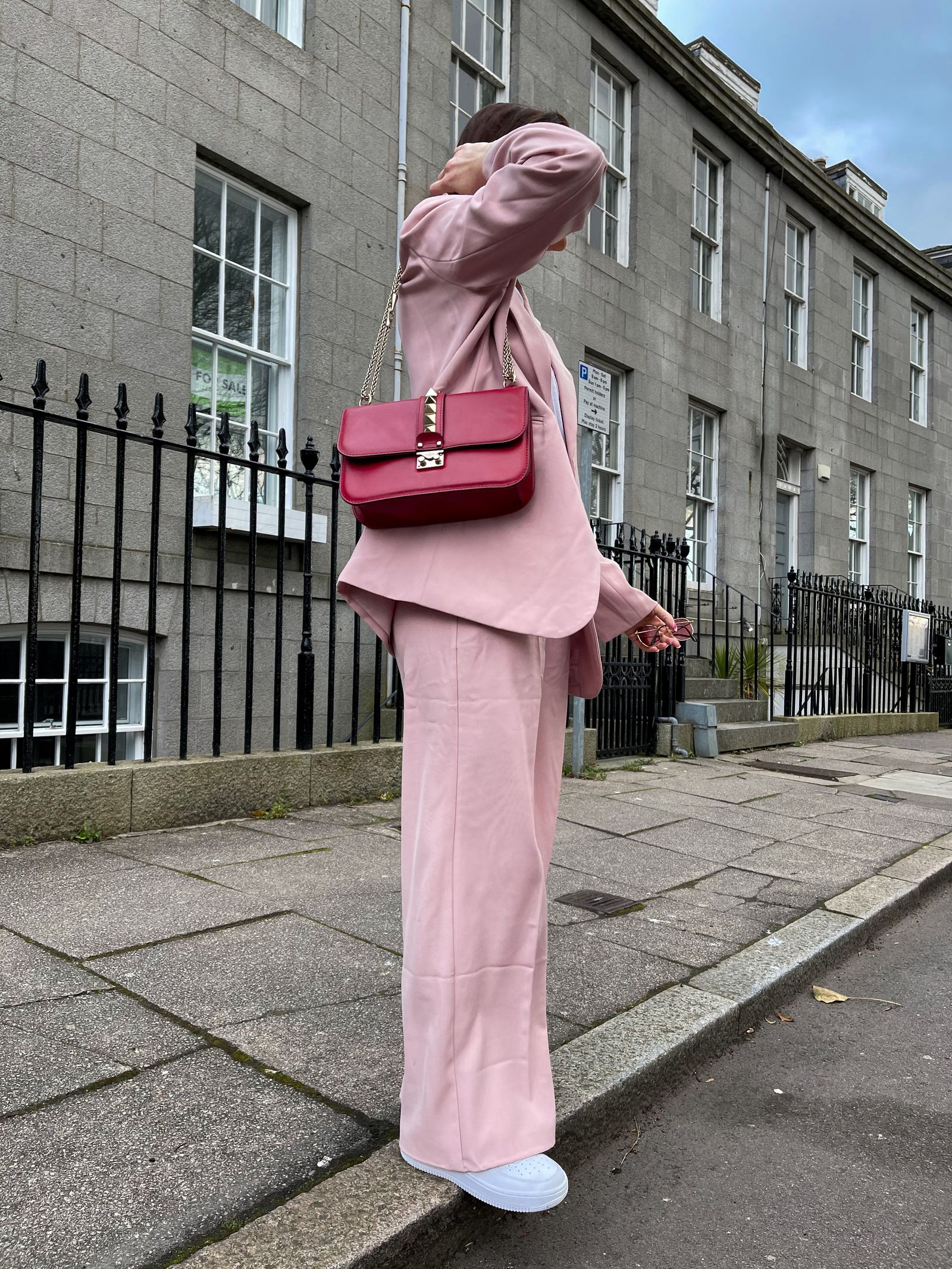 Femme en tailleur rose pâle, sac rouge à l’épaule, sur un trottoir