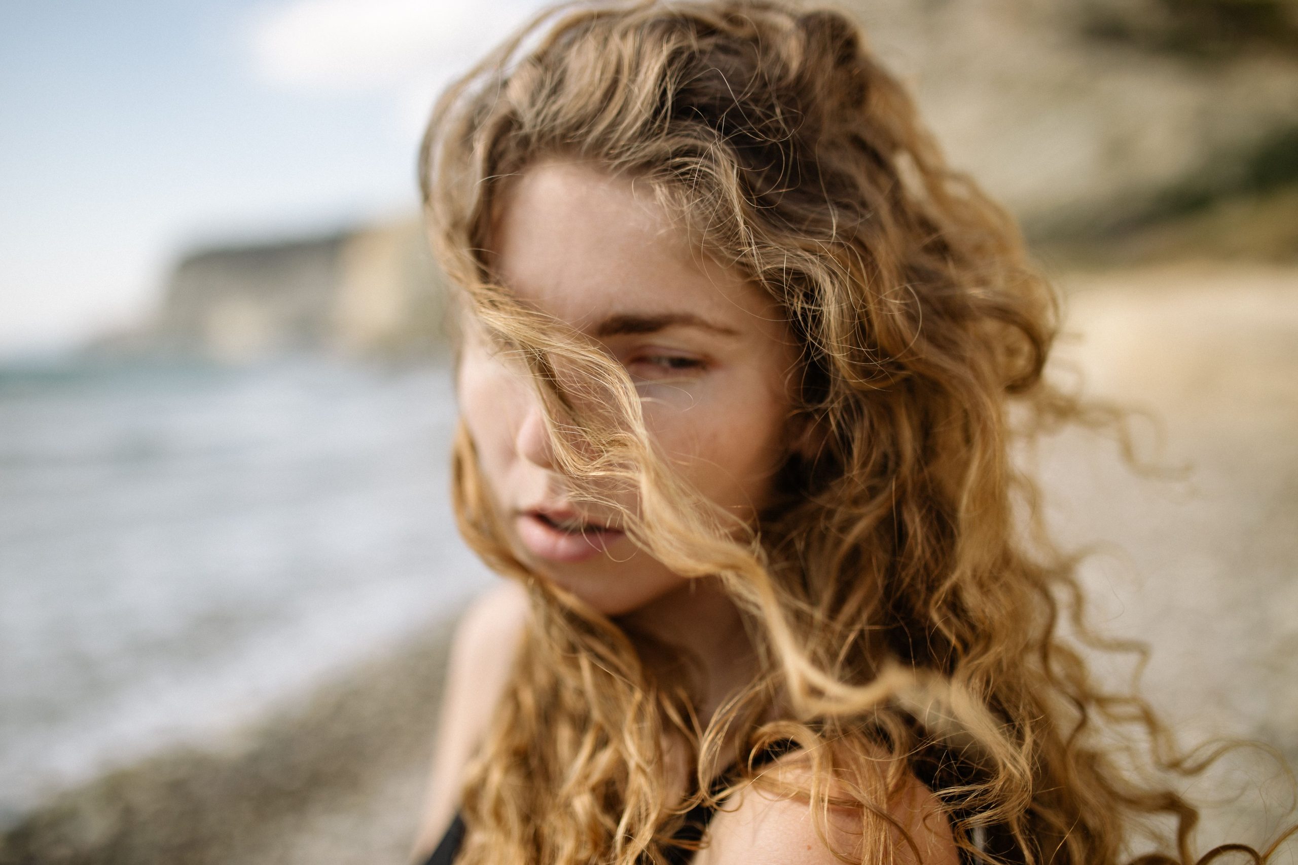 Jeune femme cheveux blonds bouclés jour venteux plage