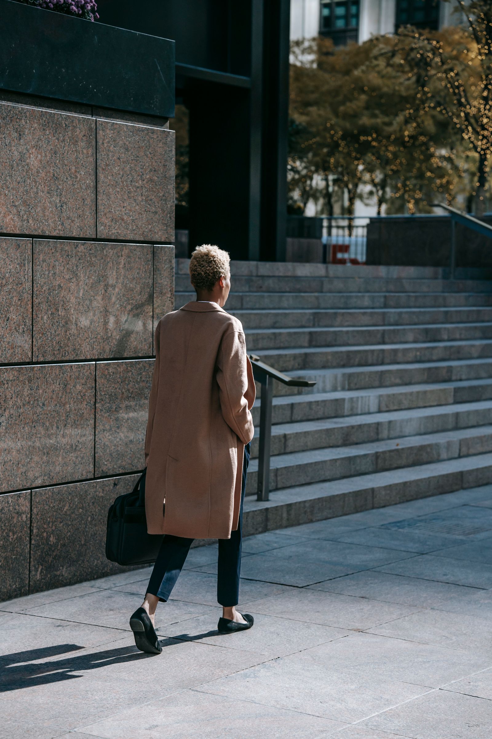 Femme en manteau beige qui monte les marches d’un immeuble
