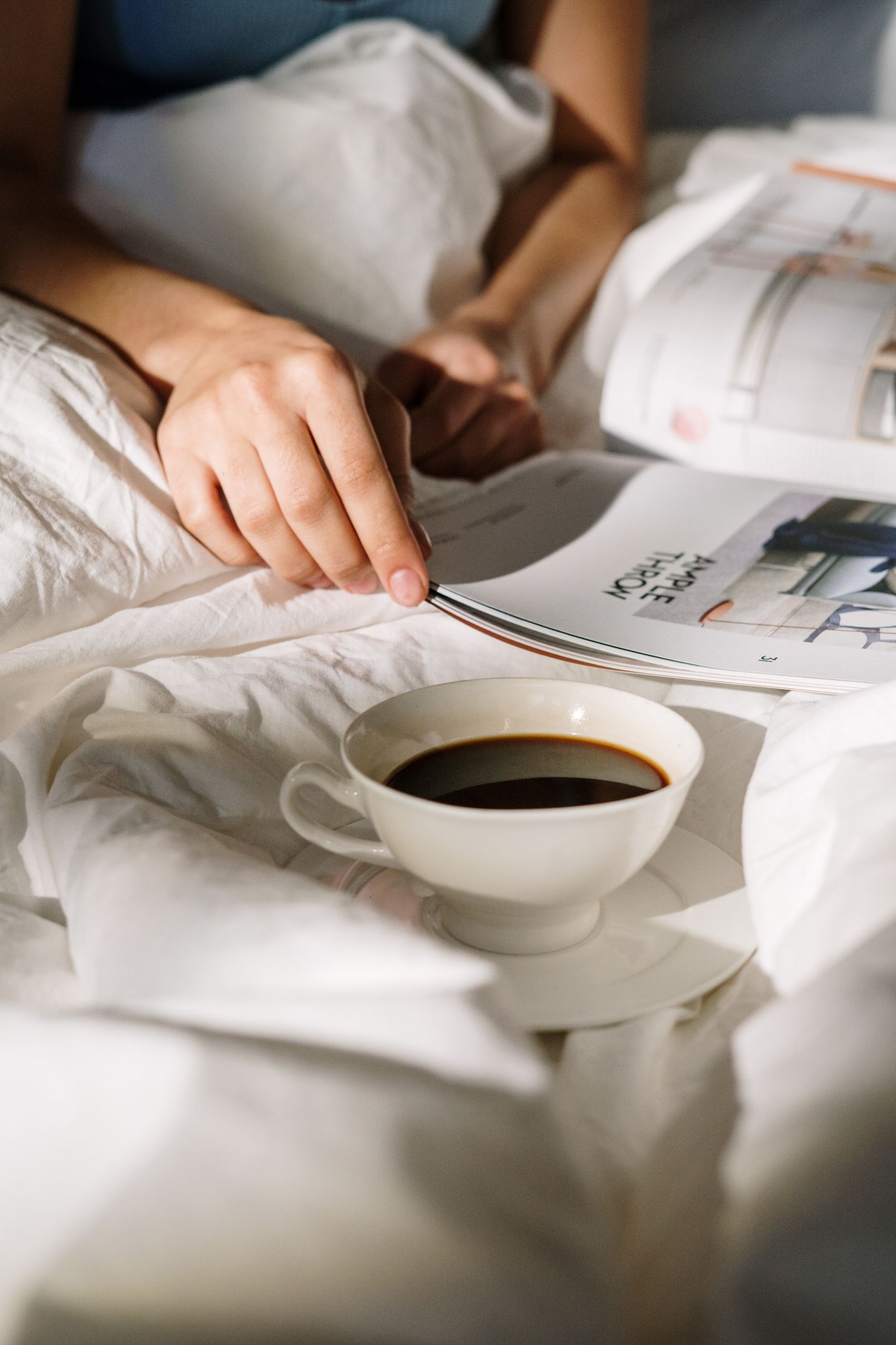 Tasse de café posée sur un magazine ouvert, dans un lit