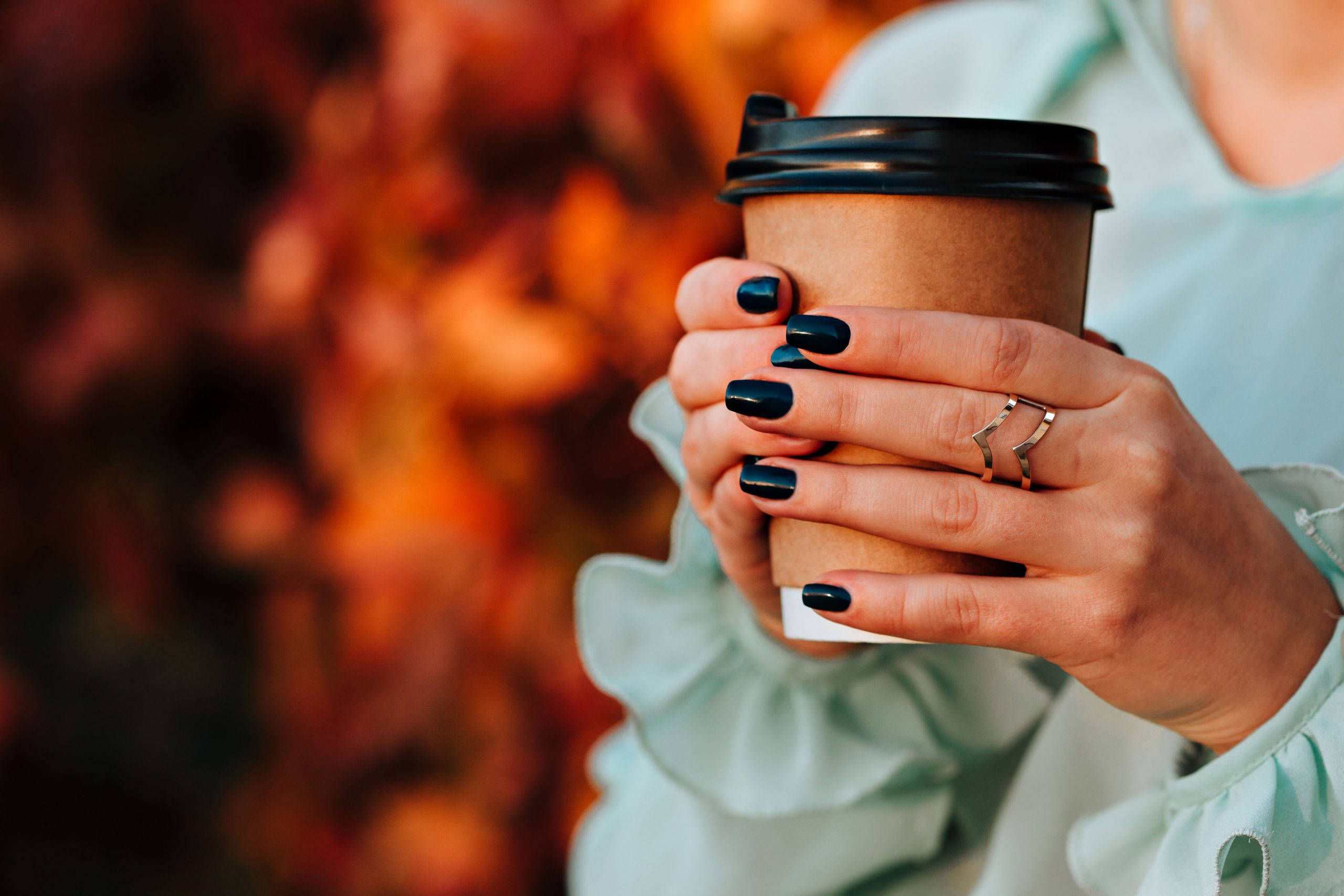 Mains vernis tenant un gobelet café automnal.