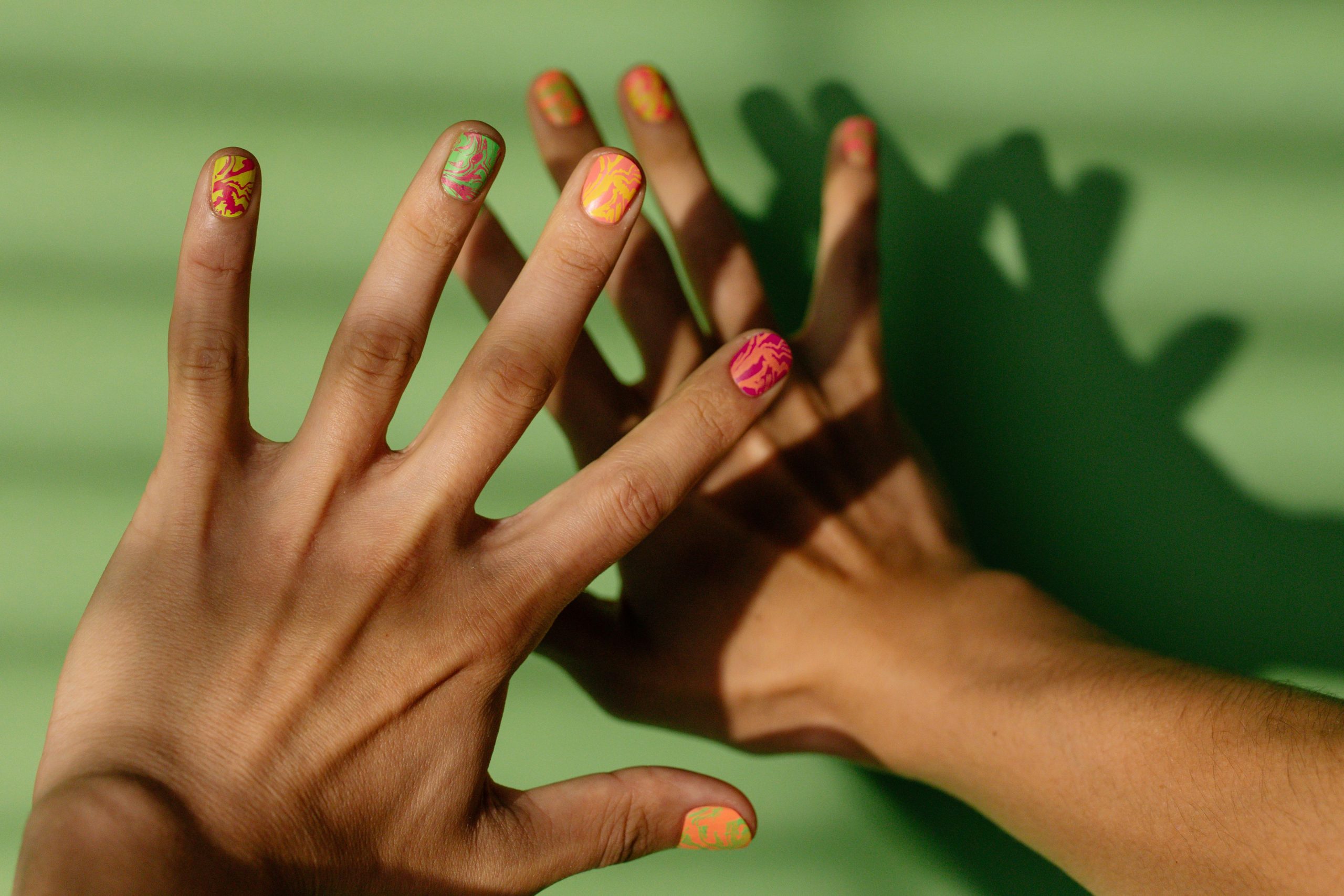 Ongles colorés projetant une ombre sur fond vert